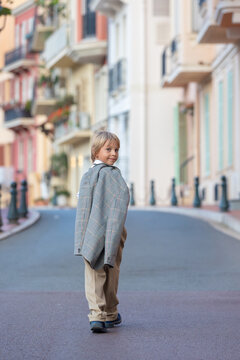 Smart casual children in suits, ties and bows,  walking on a narrow street with houses in Monaco-Ville, Monaco. Business clothing, teenagers, preschool boy and mother
