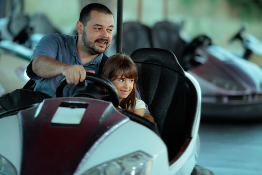 Happy Father And Daughter Driving Bumper Car At Amusement Park. Cheerful father guides his little girl while driving a bumper car together