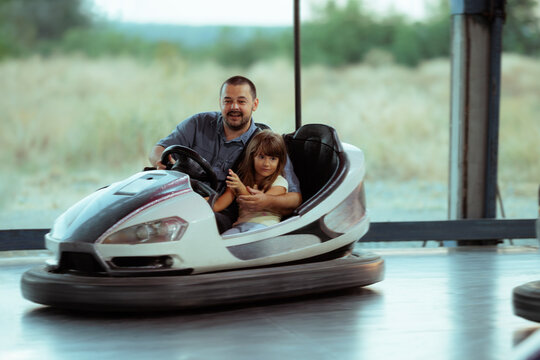Happy Father And Daughter Riding A Bumper Car At Amusement Park. Smiling father holds his little girl while driving a colorful bumper car