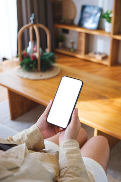 Vertical mockup image of a woman holding and using mobile phone with blank desktop white screen at home