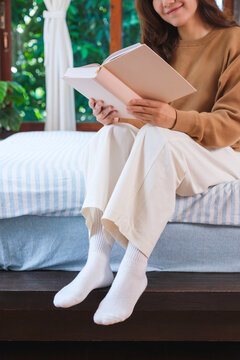 Vertical closeup image of a woman reading a book on the bed at home