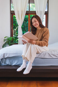 Vertical portrait image of a woman reading a book on the bed at home