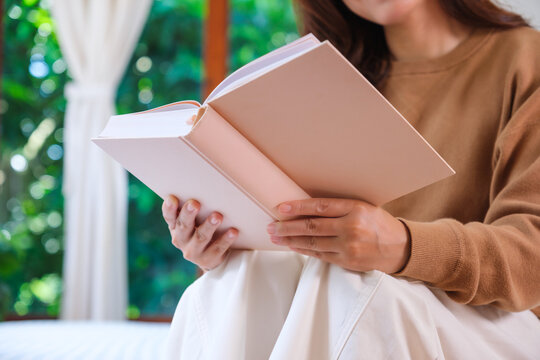 Closeup image of a woman reading a book on the bed at home