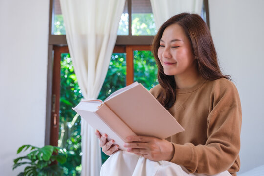 Portrait image of a woman holding and reading a book on the bed at home
