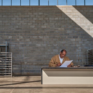 Grey breeze-block wall with copy space above a man stamping customs documents in a sunlit industrial room for trade and logistics
