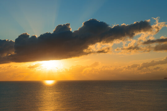 Majestic golden sunset over the calm ocean horizon with dramatic clouds and light rays at dusk