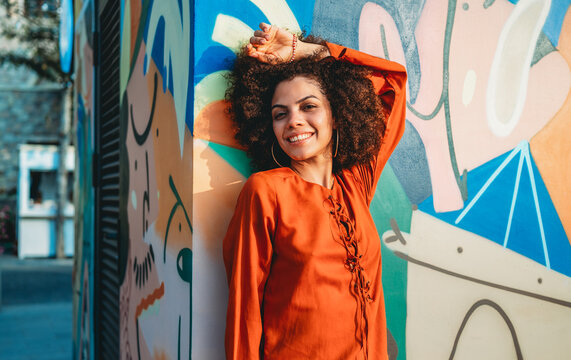 Beautiful young woman smiles warmly in a vibrant portrait against colorful street art on a sunny day