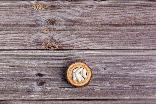 White vitamin capsules on small wooden bowl from above on wooden background in rustic. Dietary supplements, vitamins and minerals, many white pills to improve health. Happy and healthy lifestyle.