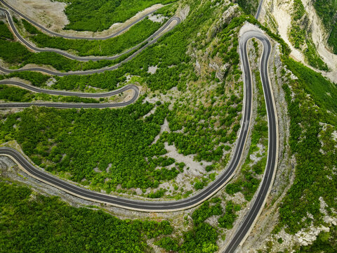 Aerial view of Leqet e Hotit winding mountain road featuring sharp hairpin turns surrounded by lush green vegetation and rocky slopes in Rrapshe, Malesi e Madhe, Shkoder County, Albania.