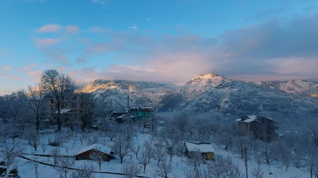 4K shot of snowy landscape after snowfall in the Himalayan mountain range in the winter season during the early morning with orange clouds as seen from Manali in Himachal Pradesh, India. 