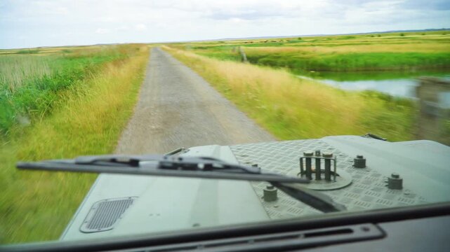 POV looking over the textured hood of an off-road military-style truck speeding along a rural countryside path. The wide open landscape creates an exciting, liberating feeling of exploration.