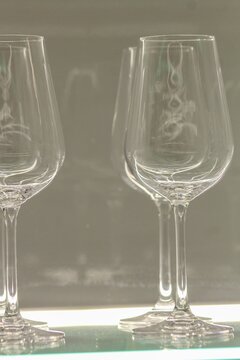 Close-up of elegant empty wine glasses displayed on an illuminated glass shelf with soft reflections and a minimalist background. Ideal for hospitality, dining, bar, restaurant, luxury, and lifestyle 