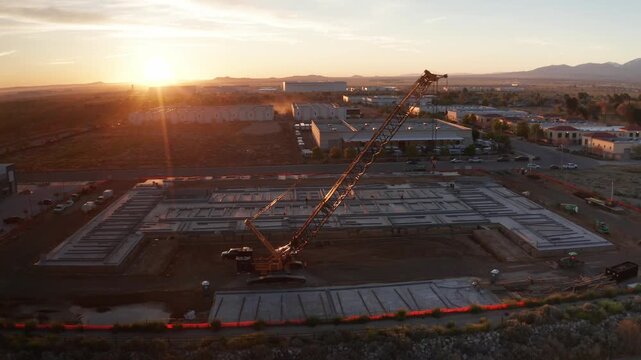 Aerial close-up panning shot of a heavy lift crane at a desert construction site with sun flare at dawn in Palmdale, California. 4K