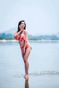 Joyful Asian woman cooling off in natural water splash during summer vacation, enjoying refreshed freedom.