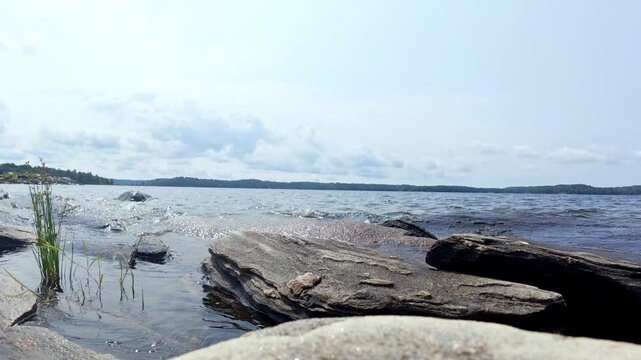 Scenic footage of freshwater waves rolling toward the shoreline of Manitoulin Island, Ontario, Canada, beneath a dramatic sky. The moving water and expansive cloud formations create an atmospheric Gre