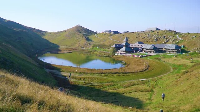 A cinematic wide establishing shot of the sacred Prashar Lake and traditional wooden pagoda temple nestled among the rolling green mountain hills of Mandi, Himachal Pradesh in North India.