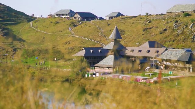 A cinematic wide establishing shot of the historic Prashar Rishi pagoda temple and traditional slate-roofed buildings nestled on a lush green mountain hillside in Mandi, Himachal Pradesh.