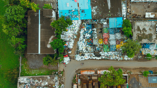 Aerial view of sorted and segregated waste piles at a waste management recycling yard with colorful plastic materials and industrial buildings in India.