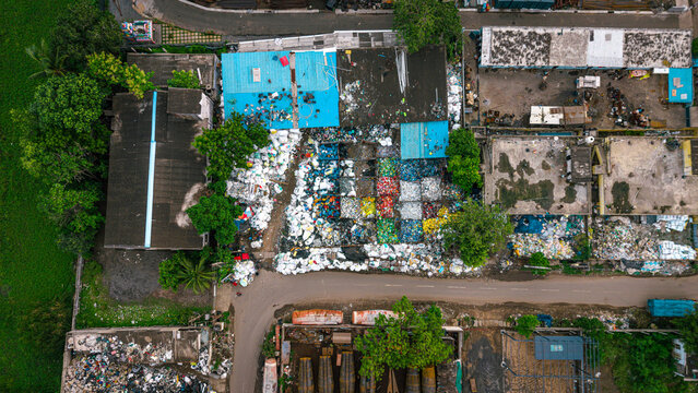 Aerial view of a waste management recycling yard featuring sorted and segregated waste piles organized in colorful sections, surrounded by industrial buildings and greenery in India.