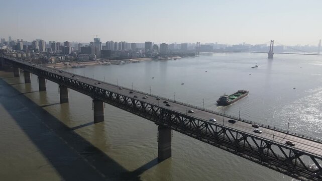 Aerial view of a double-deck steel truss bridge over a wide river with city skyline and distant suspension bridge in Wuhan, China