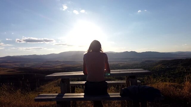 Time lapse of shirtless long haired man relaxing and doing yoga on wooden bench at sunset