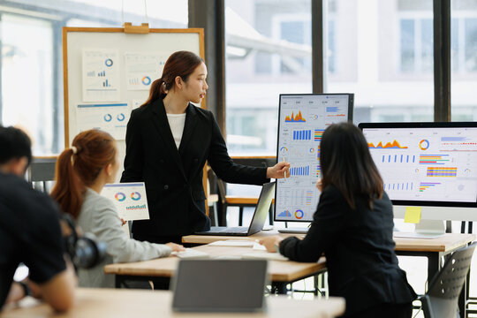 Businesswoman presenting an annual report with charts and graphs on large screens, leading a collaborative team meeting on financial growth, marketing strategy and analytics