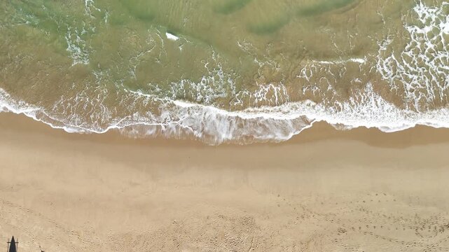 White sea waves gently roll toward a sandy beach, creating a peaceful coastal landscape. Ideal for themes of nature, ocean, travel, summer vacation, relaxation, and tropical destinations.