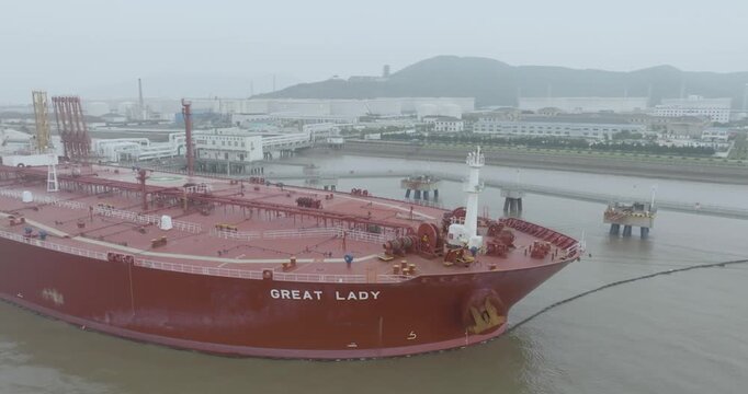 Aerial view of a large red oil tanker moored at an industrial port terminal with pipelines