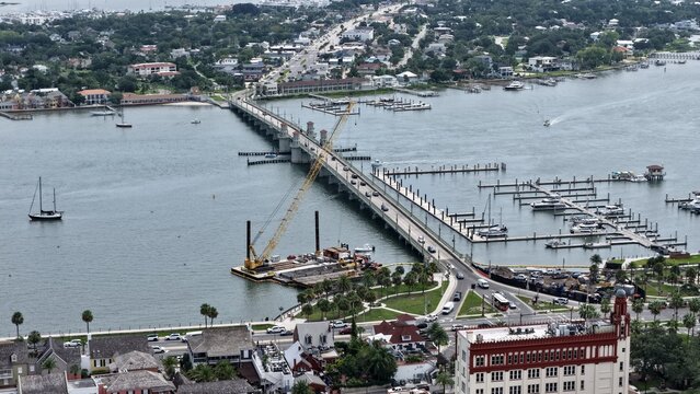 Aerial view of the Bridge of Lions with a construction crane on a barge, boats in the marina, and historic waterfront buildings in St. Augustine, Florida, United States.