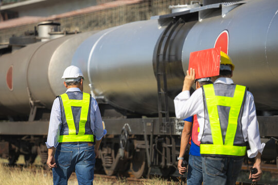 Rear view of industrial workers wearing safety equipment inspection railway transport and oil tanker wagon, Railway engineers collaborating and walking together near freight train car outdoors