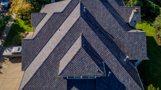 Aerial view of a residential house roof with dark shingles, a stone chimney, and surrounding green lawns in Lake Oswego, Oregon, United States.