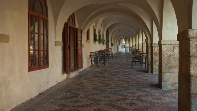 Empty outdoor cafe stands in a historic vaulted gallery with arches. Wooden tables line the quiet cobblestone arcade corridor in Prague. Great for European travel and hospitality design projects.