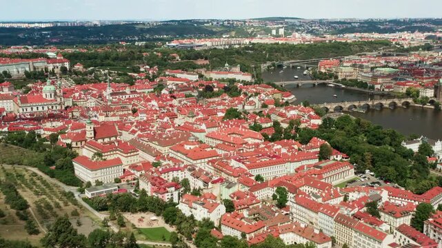 Historic Mala Strana district features red tile roofs in Prague. The Vltava River with famous Charles Bridge spans through the city. Urban architecture is a scenic landmark for Czech travel.