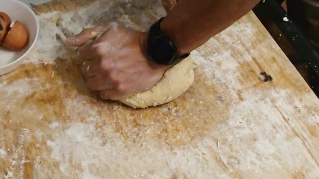 Man kneading dough with hands on floured wooden table. Homemade pastry preparation with eggshells in bowl