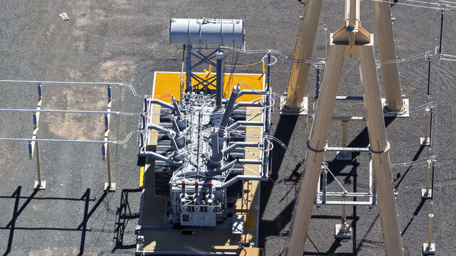 Aerial view of a large electrical transformer at a power substation with metal structures, high voltage lines, and gravel ground in Clark, Nevada, United States.