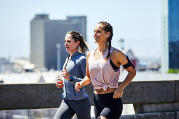 Obraz na płótnie Canvas Women, team and runner with earphones for fitness, exercise or training with hobby on road. Running, people and smile in city with tech for workout podcast, health challenge or outdoor together