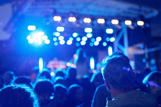 Crowd watching outdoor concert under blue stage lights at night
