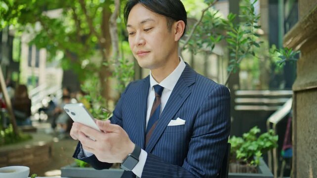 Businessman reading messages on his phone at an outdoor table
