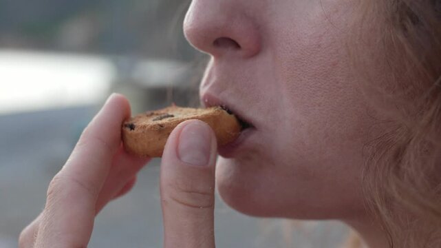 Sweet pastry nibbling by a woman outdoors near the coast, featuring a close up macro shot.