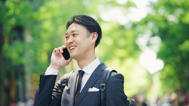 Businessman having a pleasant phone conversation on a green street
