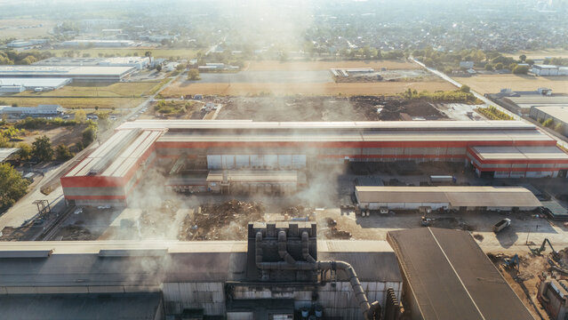 Aerial view of an industrial plant with smoke rising from the facility, surrounded by warehouses and open storage areas in Sremska Mitrovica, Vojvodina, Serbia.