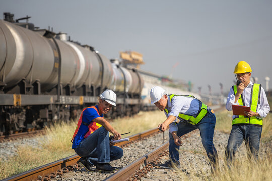 Team of engineers in safety vests and hard hats inspecting railway tracks and freight train, industrial workers with walkie talkie checking railway transport and infrastructure at cargo yard