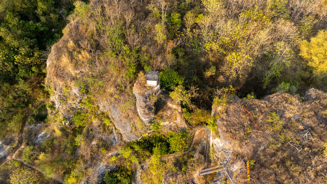 Aerial view of a rocky outcrop with a small structure surrounded by dense forest and winding paths in Klaten, Central Java, Indonesia.