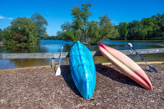 Two colorful Kayaks and paddles by an idyllic Pennsylvania lake calm water, woodland blue sky, outdoor activity couples vacation weekend travel background with copy space