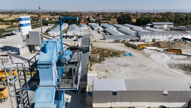 Aerial view of the TASYAPI construction facility featuring industrial silos, blue machinery, rows of modular buildings, and trucks on a gravel site in Kuzmin, Vojvodina, Serbia.