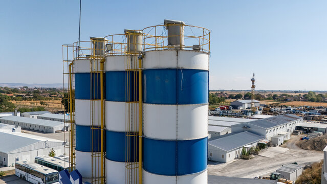 Aerial view of TASYAPI industrial site featuring blue and white silos with yellow ladders, surrounded by warehouse buildings and construction equipment in Kuzmin, Vojvodina, Serbia.