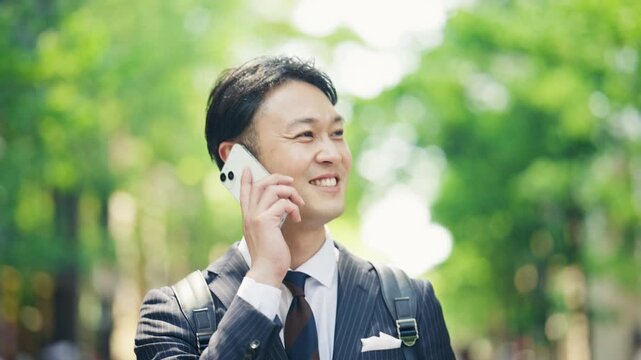 Japanese businessman smiling during a phone call among fresh greenery