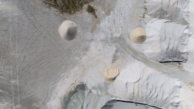 Aerial view of a gravel quarry with large piles of sand and aggregate, tire tracks on the ground, and industrial textures in Kuzmin, Vojvodina, Serbia.