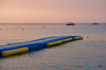 Floating modular plastic pontoon pier on calm sea water at sunrise with speedboats in background © Vivid Moments