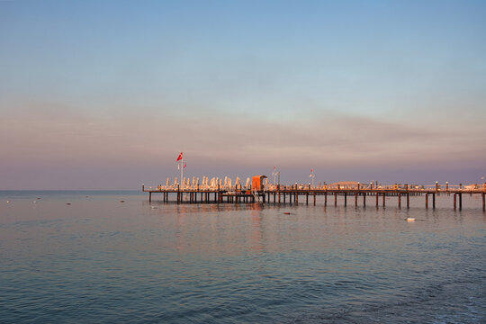 Long wooden resort pier on stilts over calm sea with Turkish flag at sunrise